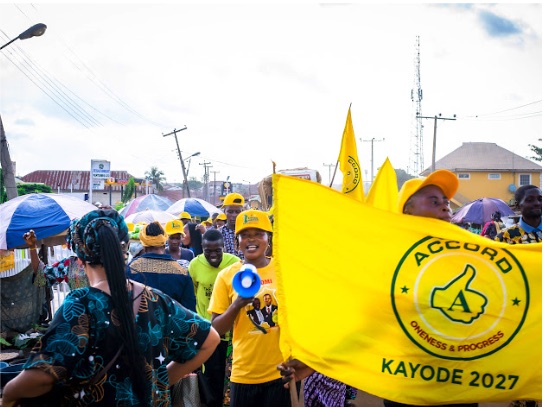 A supporter with a megaphone beside a large ACCORD Kayode 2027 flag